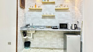 A compact kitchen with white brick walls, a granite countertop, a microwave, a kettle, and two shelves with jars and a plant. - La Casa del Centro Cairo (Cairo)