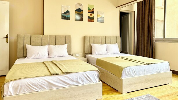 A hotel room with two beds, beige walls, and artwork on the wall. - La Casa del Centro Cairo (Cairo)