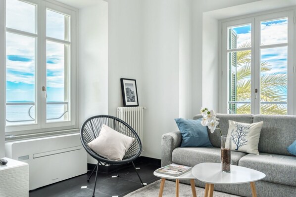 A modern living room with a grey sofa, a black chair, and a white coffee table. There is a framed picture on the wall and a radiator below it.