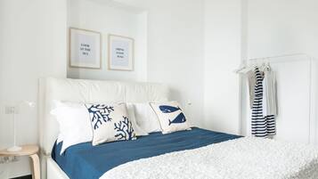 A neatly arranged bedroom with a bed, pillows, a bedside table, and a wall-mounted towel rack.