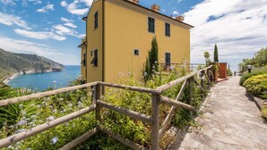 A yellow building with a stone pathway and wooden railing, overlooking a coastal area with cliffs and the sea.