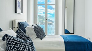 A bedroom with a bed, a window with a view of a mountainous landscape, a framed picture on the wall, and a mirror.