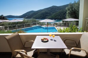 A balcony with a table, chairs, and a view of a swimming pool and mountains. - ROUDA VILLAGE (Lefkada)