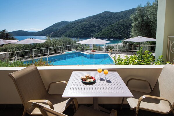 A balcony with a table, chairs, and a view of a swimming pool and mountains.