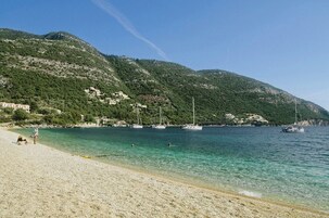 Μια παραλία με κρυστάλλινα, γαλαζοπράσινα νερά, βάρκες και κτίρια χτισμένα σε μια πλαγιά λόφου.