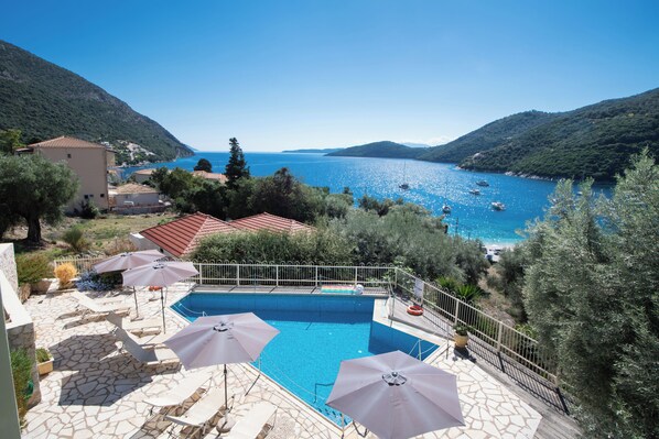 A swimming pool with umbrellas, stone flooring, and a view of the sea and hills. - ROUDA VILLAGE (Lefkada)