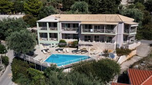A two-story building with a swimming pool, outdoor seating, and a stone wall. - ROUDA VILLAGE (Lefkada)