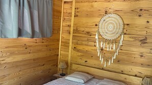 Ein Schlafzimmer einer Holzhütte mit einem Bett, einer Hängelampe, einer Wanddekoration und einem Fenster mit Vorhängen.