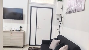 A living room with a black sofa, a TV, a wooden cabinet, and a door with a window. - Domus Tiziano: Elegant Living Room 30m from Metro C - Center of Rome (Roma)