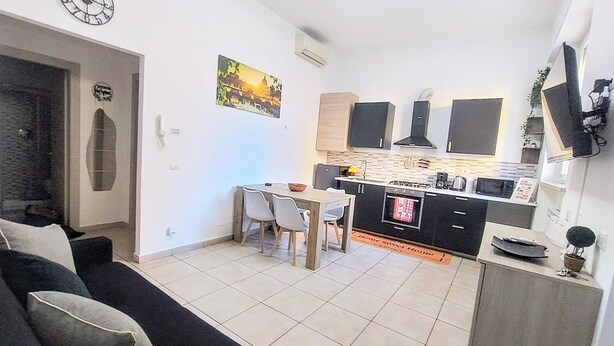 A modern kitchen with a dining area, a black sofa, and a clock on the wall. - Domus Tiziano: Elegant Living Room 30m from Metro C - Center of Rome (Roma)