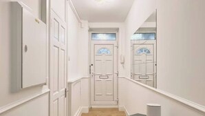 A narrow hallway with white walls and wooden flooring. There is a door at the end of the hallway with a small window above it. A white object is placed on a small table at the end of the hallway. - Spacious 3-bed Apartment by Stockwell Station (London)