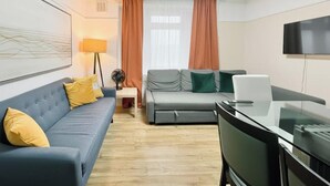 A modern living room with a sofa, a smaller couch, a glass table, and a TV on the wall. - Spacious 3-bed Apartment by Stockwell Station (London)
