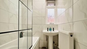 A bathroom with a bathtub, a sink, and a window. - Spacious 3-bed Apartment by Stockwell Station (London)