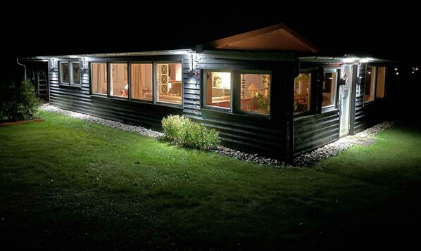 Un bâtiment de style chalet en bois, doté de grandes fenêtres, d’un porche couvert et d’une pelouse bien entretenue.
