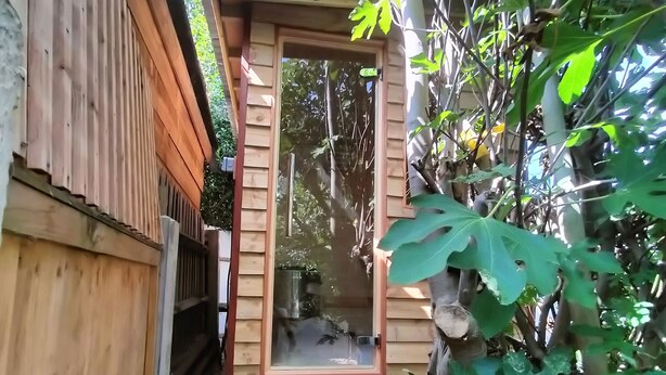 A wooden structure with a glass door, a small wooden staircase, and a blue bucket on the ground. - Artist house with garden sauna in London (London)