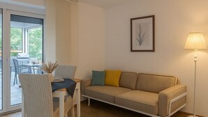 Een moderne woonkamer met een bank, een eettafel, stoelen, een kamerkleed met patroon, een lamp en een lijst met kunstwerk aan de muur.