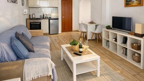 Een moderne woonkamer met een bank, salontafel, televisie en een keuken op de achtergrond.