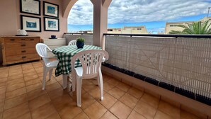 En balkon med dug i tern, to hvide stole, et træskab og billeder i rammer på væggen.