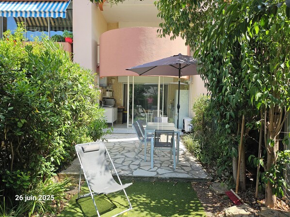 A patio area with a table and chairs, a folding chair, and a large umbrella. - 40m², 100m from beach, garden, 1 bedroom, living room (sofa bed), fiber box, air conditioning, no pets (La Ciotat)