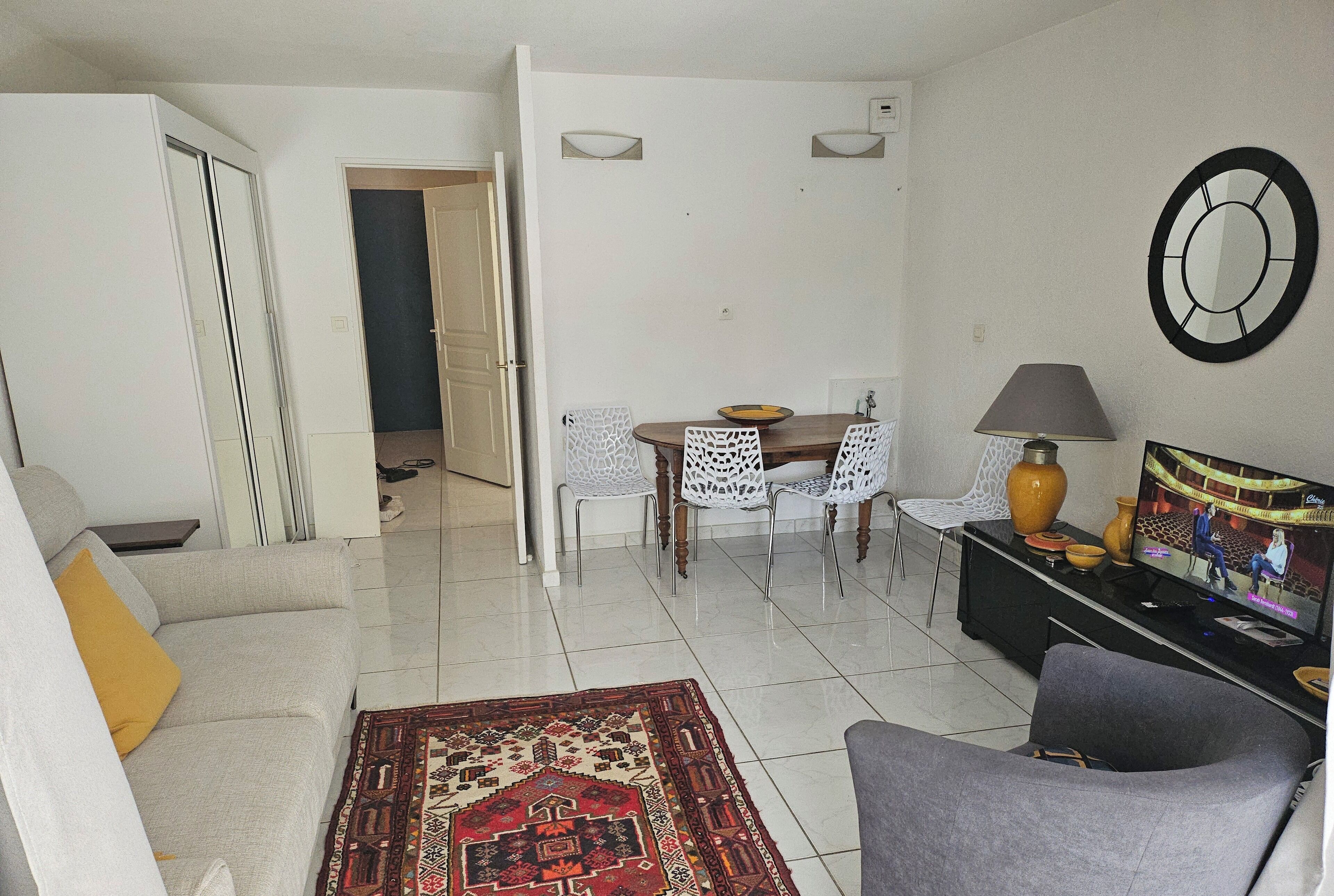 A living room with a sofa, a coffee table, a TV, and a dining area with chairs and a table.