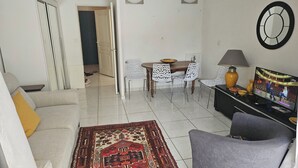 A living room with a sofa, a coffee table, a TV, and a dining area with chairs and a table. - 40m², 100m from beach, garden, 1 bedroom, living room (sofa bed), fiber box, air conditioning, no pets (La Ciotat)