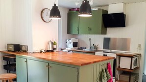 Une cuisine avec un îlot central en bois, des armoires vertes, une horloge et un four à micro-ondes.