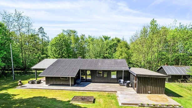 Une maison moderne dotée d’une grande terrasse, d’un espace salon extérieur abrité et d’un petit jardin.