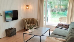 Un salon doté d’un téléviseur à écran plat, d’un fauteuil à rayures, d’un canapé, d’une table basse et offrant une vue sur la verdure environnante.