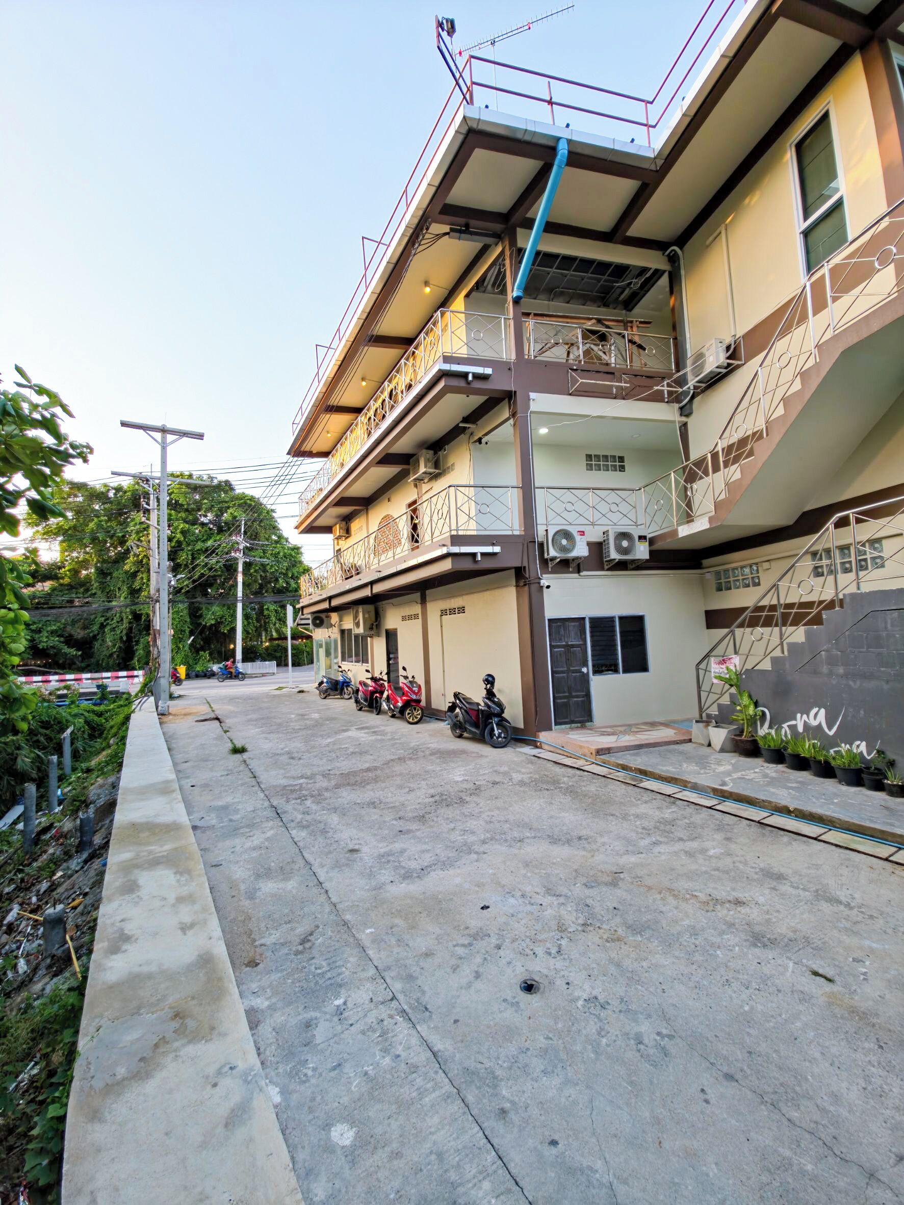 A multi-story building with balconies, a covered parking area, and a row of parked motorcycles.