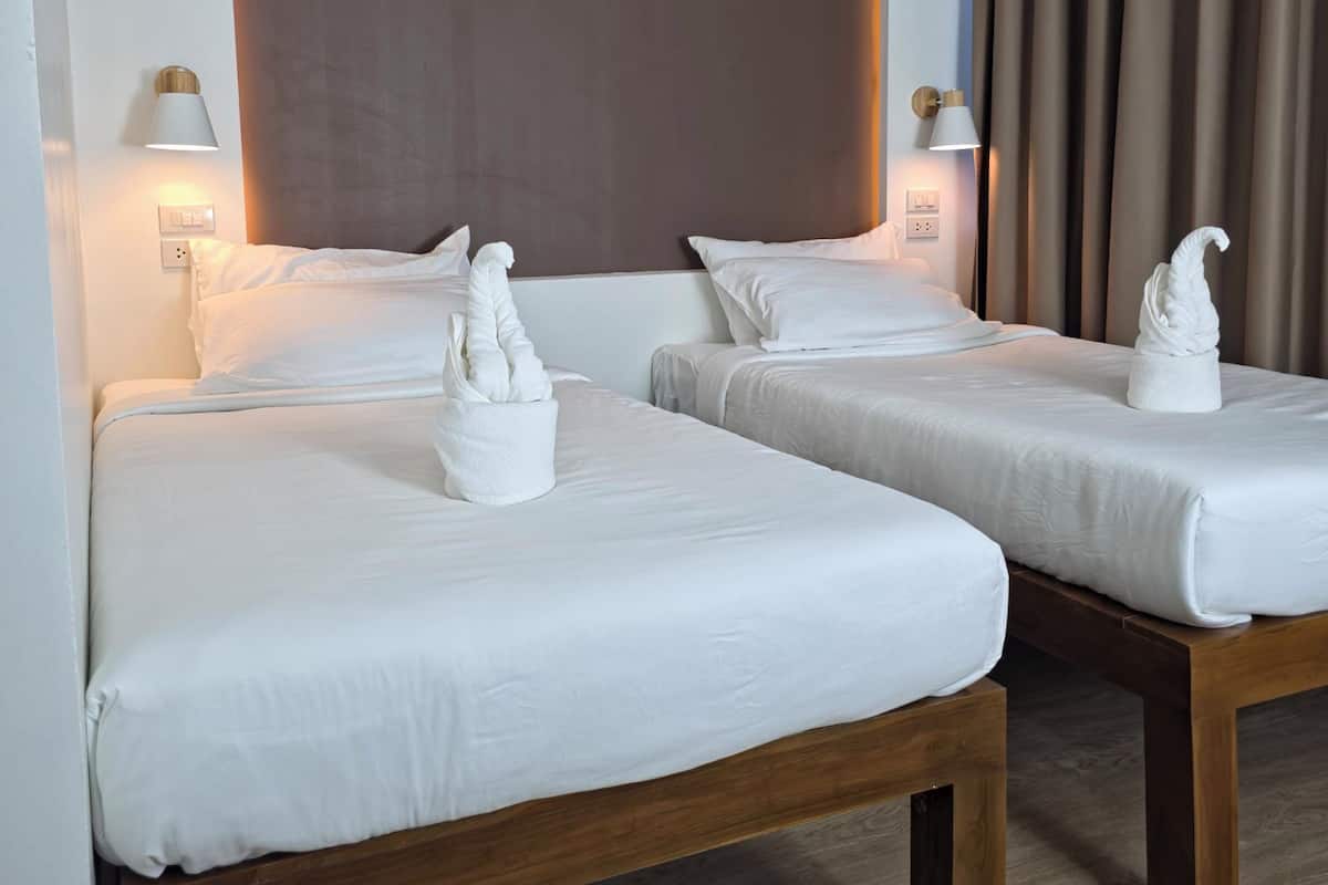 Hotellihuone, jossa on kaksi sänkyä, puinen pääty ja seinään kiinnitetyt lamput.