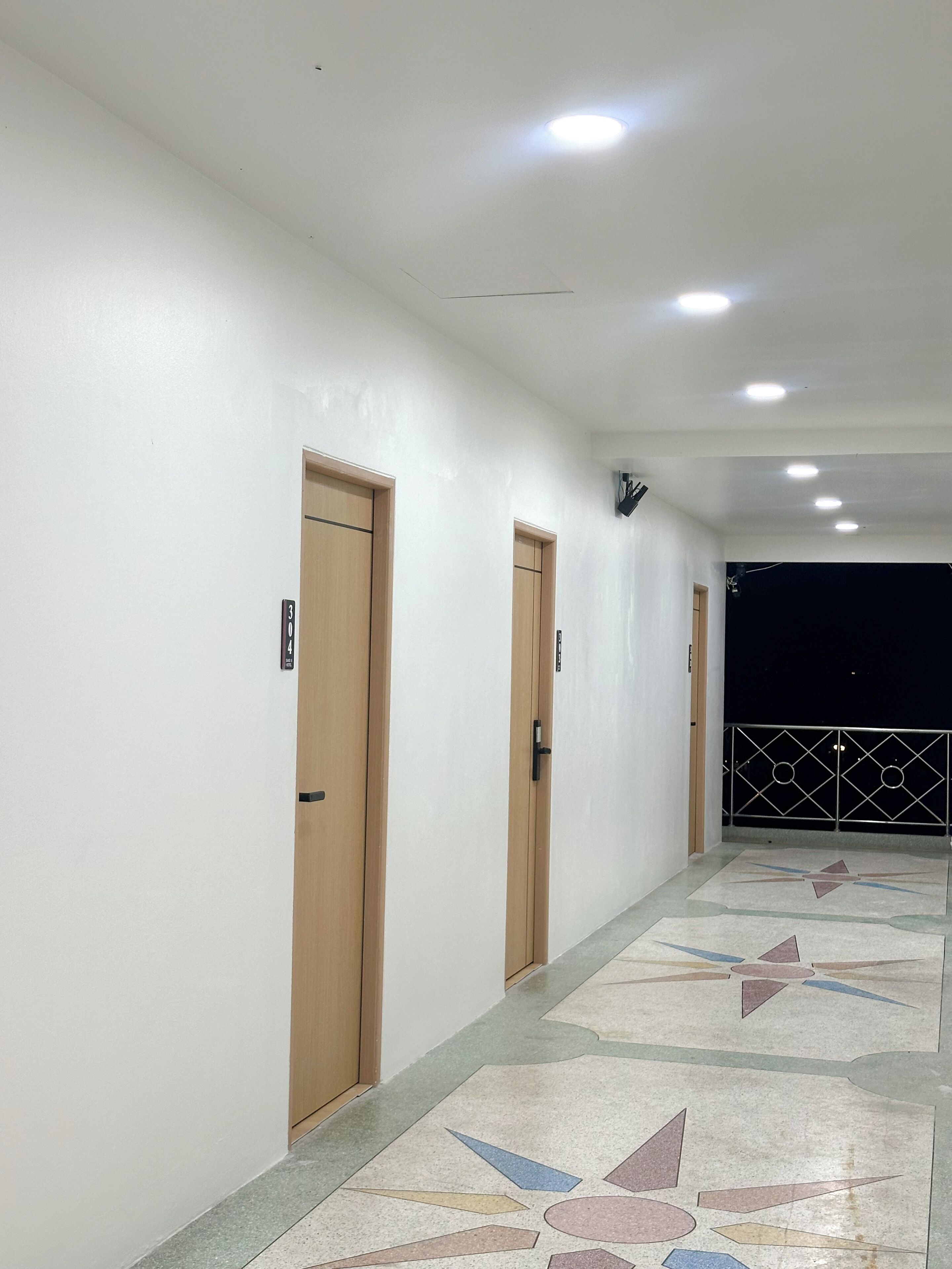 A corridor with doors, a tiled floor, and a balcony with a railing.