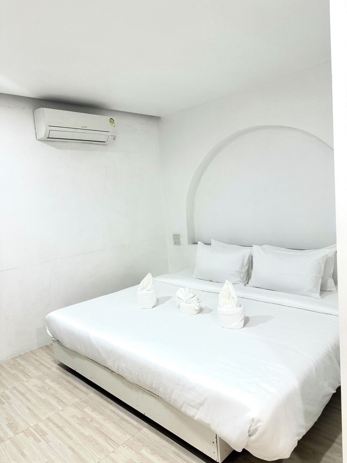 Habitación de hotel con cama, ropa blanca, aire acondicionado de pared y un diseño sencillo y limpio.