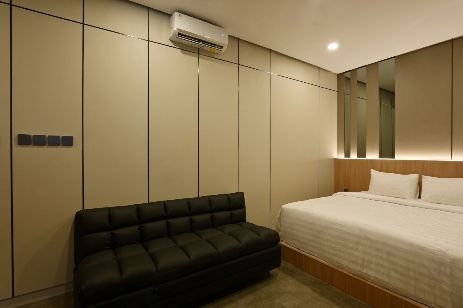A modern bedroom with a bed, a black sofa, and a wall-mounted air conditioner.