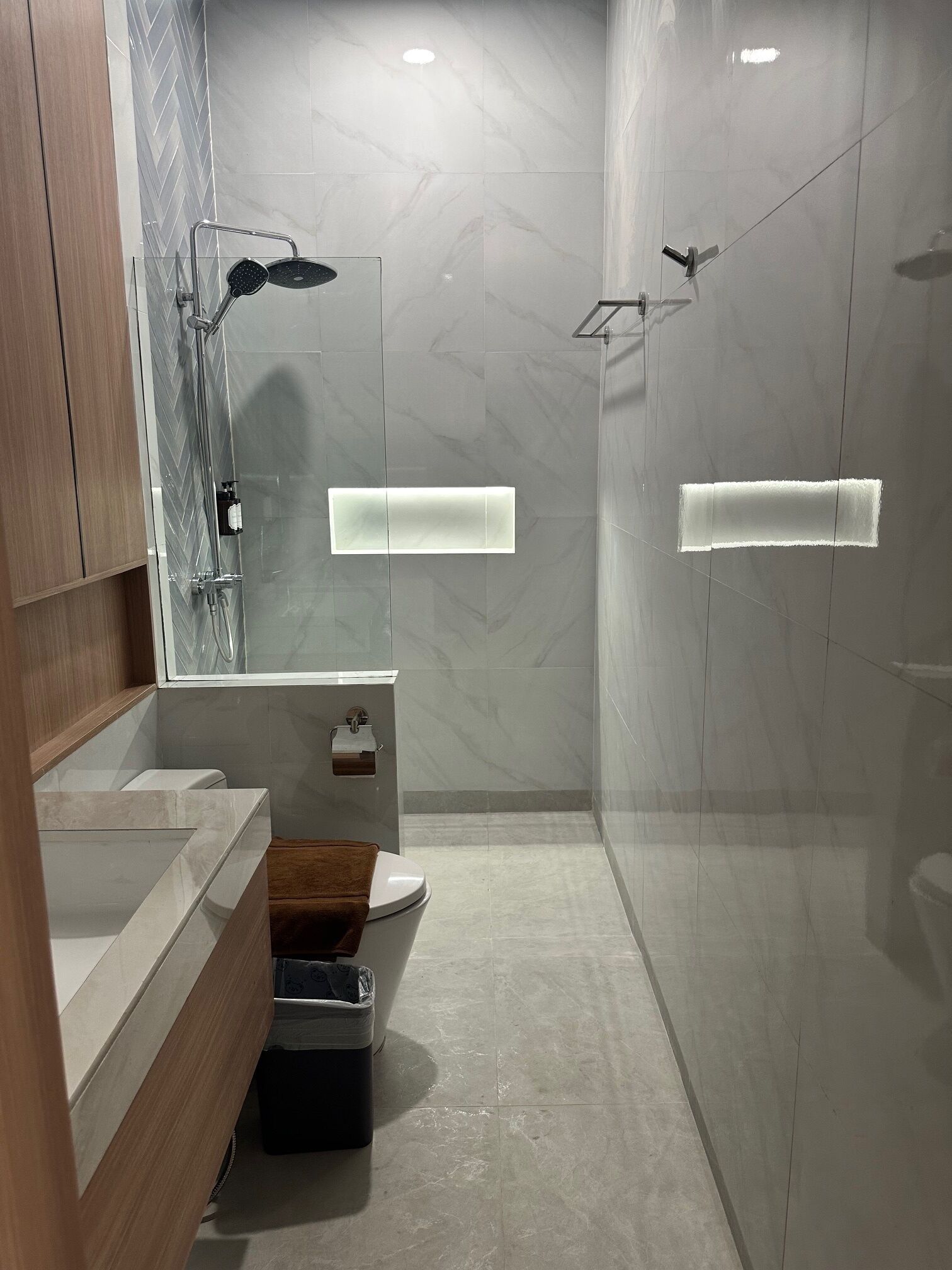 A modern bathroom with a glass-enclosed shower, a wooden vanity with a mirror, and a toilet.