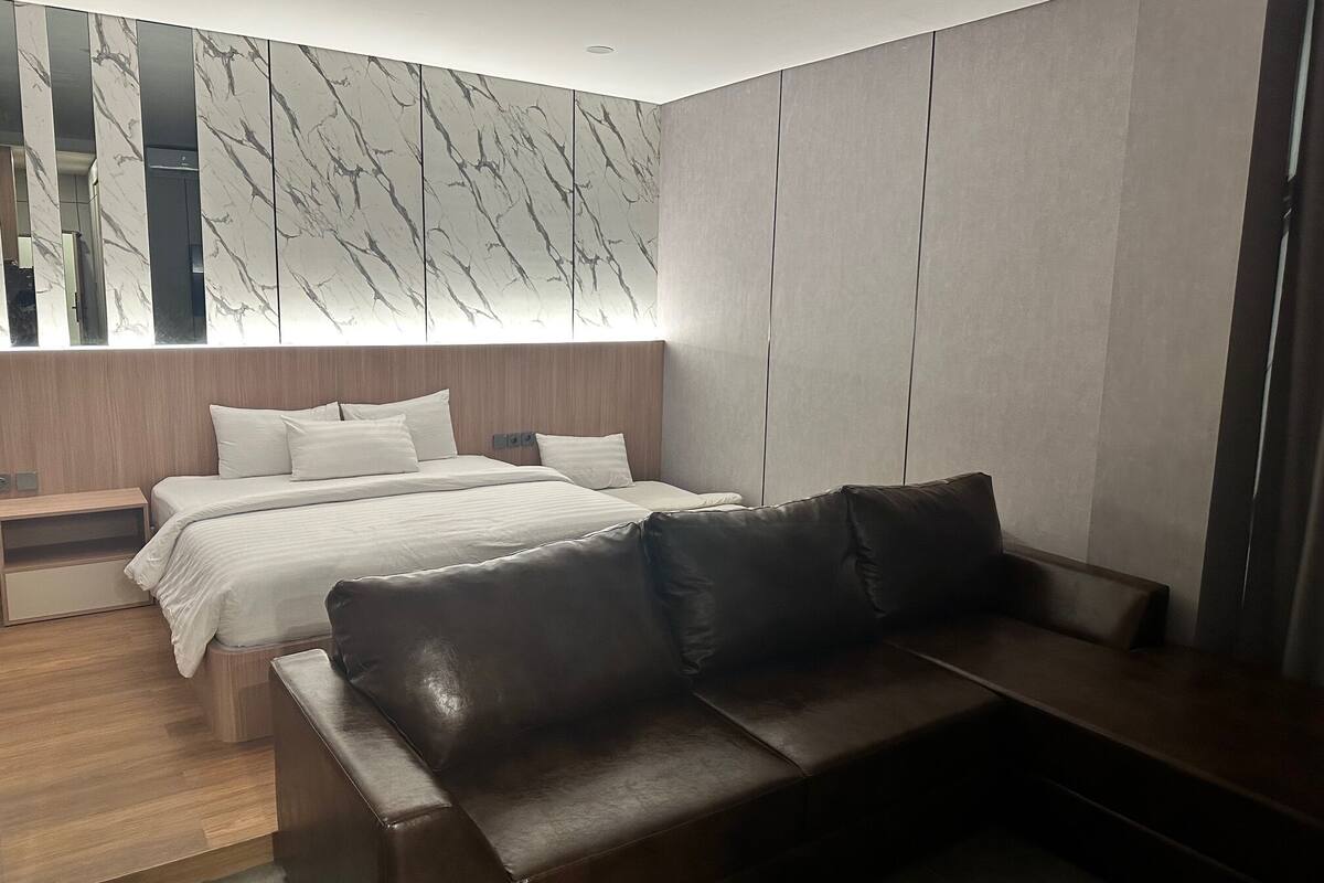A modern bedroom with a large bed, a sofa, a nightstand, and a wall with a marble-like pattern.