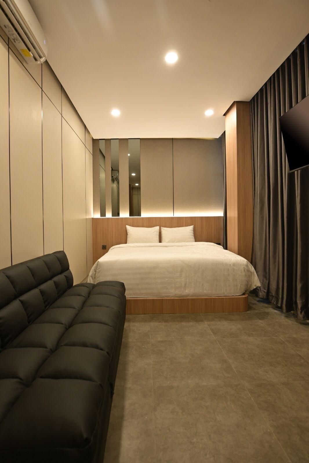 Un dormitorio moderno con cama, sofá, televisor y espejo.