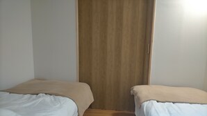 A room with two single beds, a wooden wardrobe, and a wooden floor.