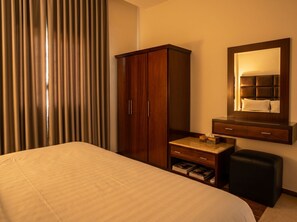 A hotel room with a bed, a wooden wardrobe, a vanity with a mirror, and a small stool. - Vinas Riyadh Serviced Apartments (Riyadh)