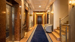 A hotel hallway with a blue carpet, marble walls, and a staircase with metal railings. - Vinas Riyadh Serviced Apartments (Riyadh)