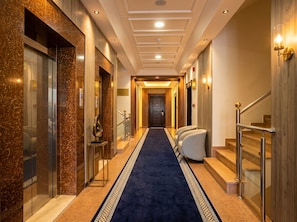 A hotel hallway with a blue carpet, marble walls, and a staircase with metal railings. - Vinas Riyadh Serviced Apartments (Riyadh)