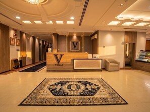 A hotel reception area with a reception desk, a carpeted floor, and a wall-mounted air conditioning unit. - Vinas Riyadh Serviced Apartments (Riyadh)