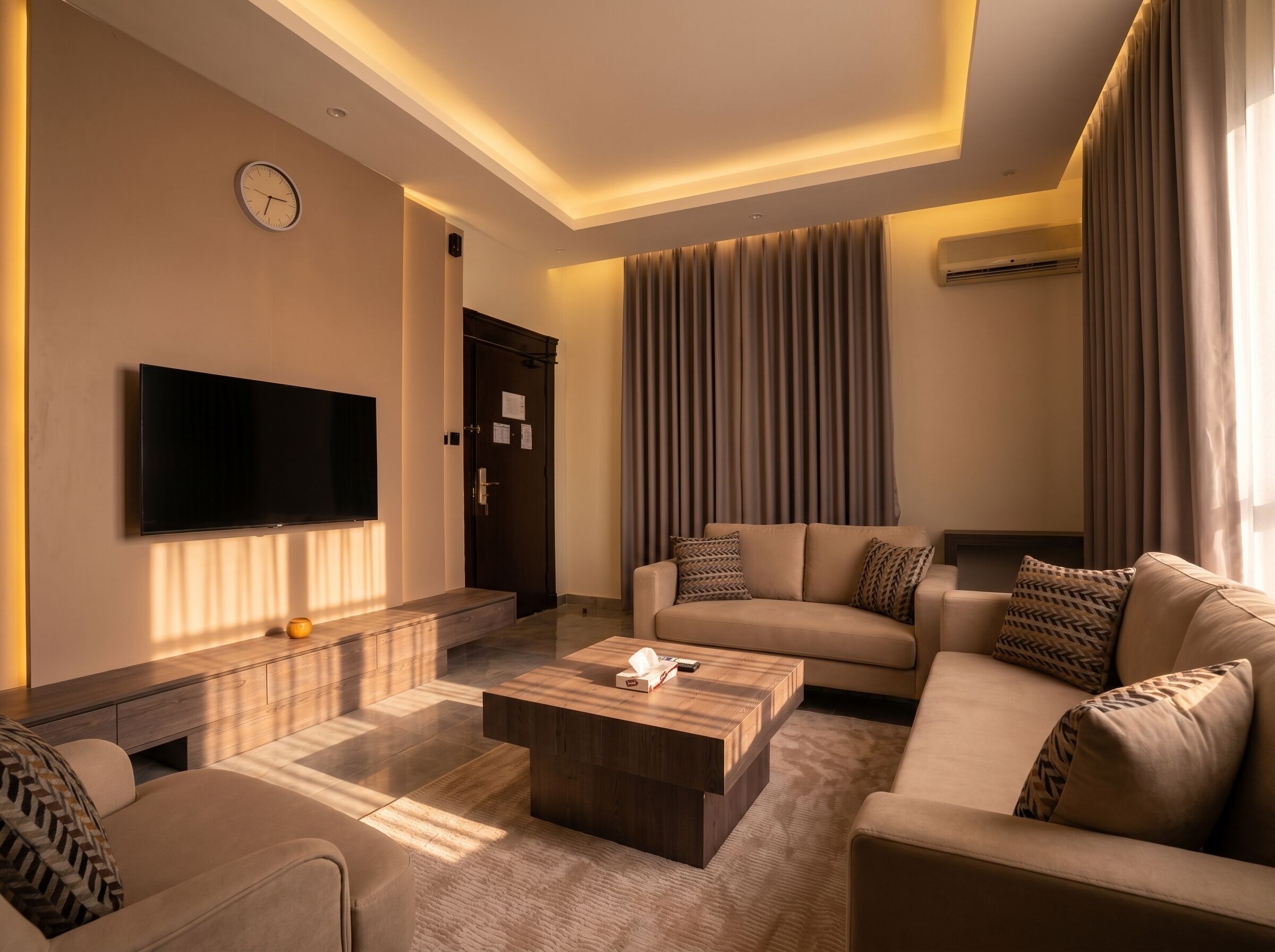 Una sala de estar moderna con una televisión de pantalla plana, un sofá, una mesa de centro y un ventanal con cortinas.