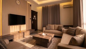 A modern living room with a flat-screen TV, a sofa, a coffee table, and a large window with curtains. - Vinas Riyadh Serviced Apartments (Riyadh)