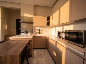 A modern kitchen with a wooden table, a built-in microwave, and a coffee maker. - Vinas Riyadh Serviced Apartments (Riyadh)
