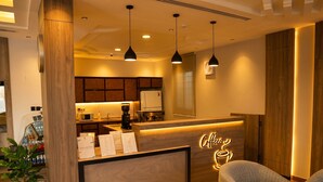 A modern coffee shop interior with a wooden reception desk, pendant lighting, and a seating area with a sofa and table. - Vinas Riyadh Serviced Apartments (Riyadh)