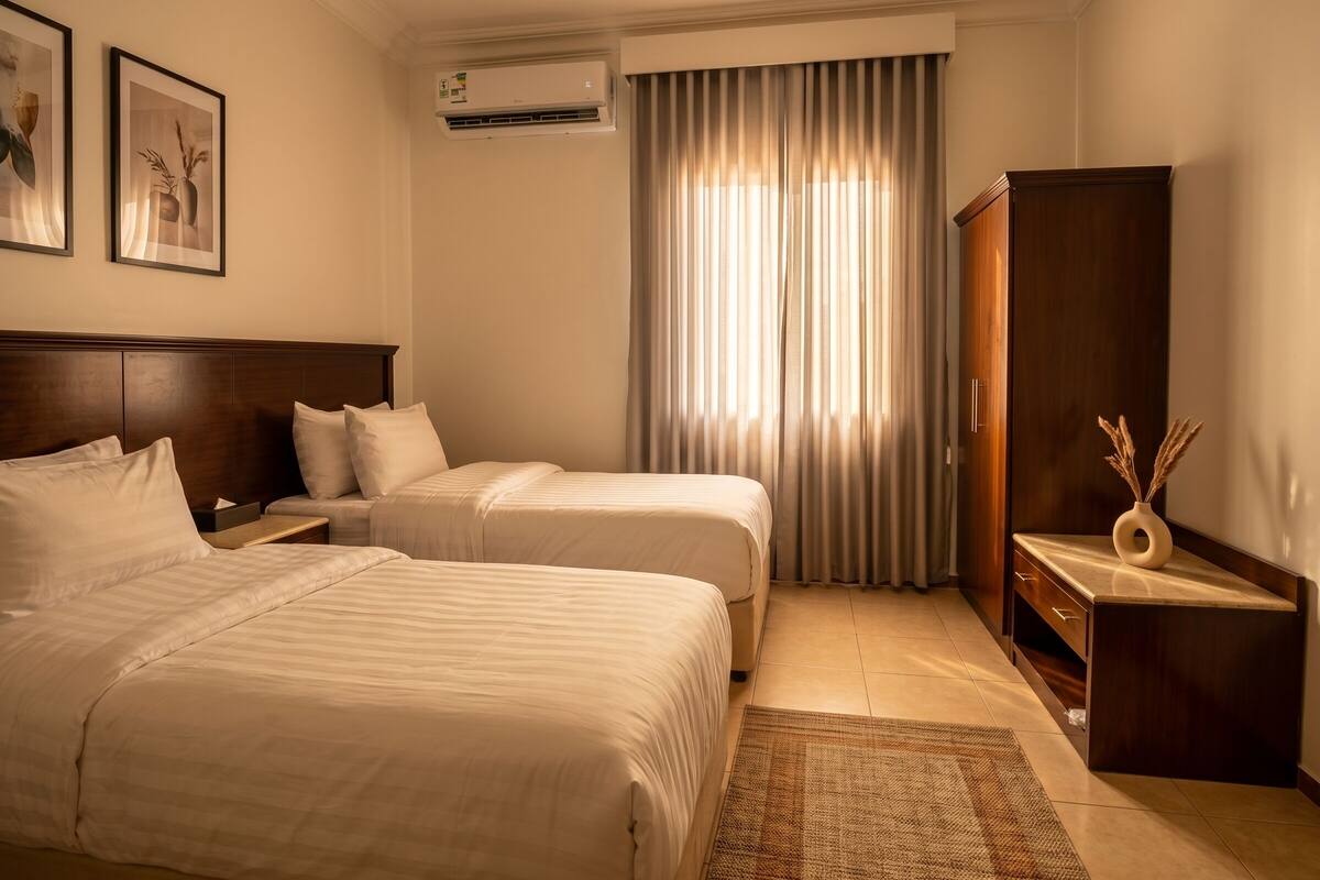 Ein Hotelzimmer mit zwei Betten, einem Holzschrank, einem kleinen Tisch und einer Klimaanlage.