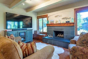 A living room with a large flat-screen TV, a fireplace, and a view of the outdoors. - Villager Condo 1242 - Cozy & Close to Dollar Mountain Skiing (Sun Valley)
