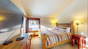 Ein Schlafzimmer mit einem Bett, einem Schreibtisch mit Fernseher, einem Sessel und einer Lampe.