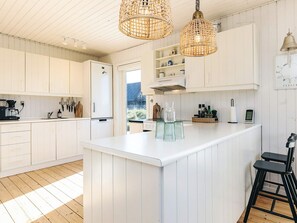 A modern kitchen with white cabinetry, a central island, hanging wicker light fixtures, and a view of the outdoors. - 4 Star Holiday Home in Skagen (Skagen)