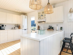 A modern kitchen with white cabinetry, a central island, hanging wicker light fixtures, and a view of the outdoors.